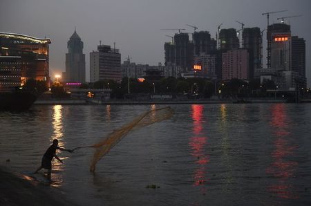 © Reuters. A man casts a net by the side of a river next to a construction site of new residential buildings in Wuhan