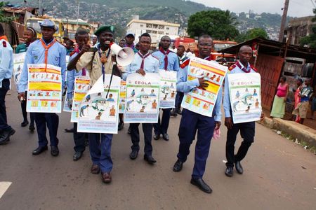 © Reuters. Members of a UNICEF-supported social mobilization team walk on a street, carrying posters with information on the symptoms of Ebola in Freetown