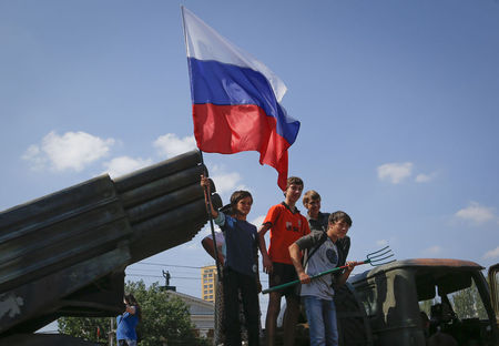© Reuters. Children holding a Russian flag pose for photos on a destroyed Ukrainian army Grad multiple rocket launcher system that was seized and put on public display at the central square in Donetsk