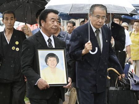 © Reuters. Mikio Watanabe, holding a portrait of his late wife Hamako, walks into the Fukushima District Court in Fukushimaima