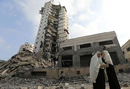 © Reuters. Palestinian women stand next to the remains of one of Gaza's tallest apartment towers, which witnesses said was hit by an Israeli air strike that destroyed much of it, in Gaza City