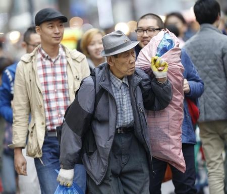 © Reuters. Man collecting recyclable goods carries bags as people walk to shop in central Seoul