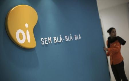 © Reuters. A woman stands next to the logo of Brazil's largest fixed-line telecoms group Oi, inside a shop in Sao Paulo