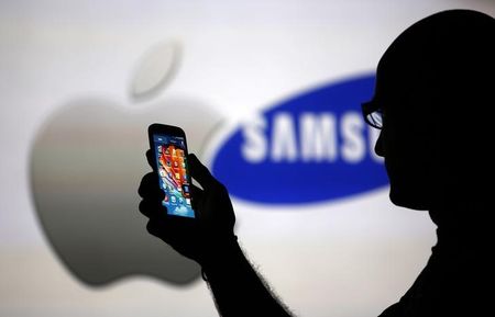 © Reuters. A man is silhouetted against a video screen with Apple and Samsung logos as he poses with a Samsung Galaxy S4 in this photo illustration taken in the central Bosnian town of Zenica