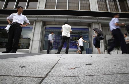 © Reuters. Pedestrians walk past an electronic board showing Japan's Nikkei average outside a brokerage in Tokyo