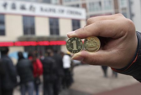 © Reuters. A resident displays newly-issued one Chinese yuan souvenir coins, to commemorate the Year of the Horse, as people queue to exchange the coins outside a Bank of China branch in Neijiang