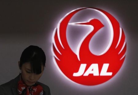 © Reuters. An employee of Japan Airlines works next to the company logo at Haneda Airport in Tokyo