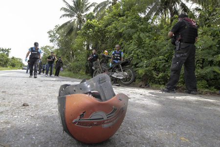 © Reuters. A helmet lies along a roadside as Thai security personnel inspect the site of a bomb attack in Pattani province