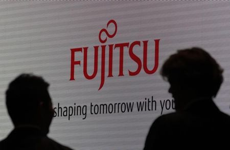 © Reuters. People are silhouetted against screen displaying logo of Fujitsu at CEATEC JAPAN 2012 electronics show in Chiba