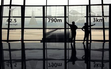 © Reuters. Two people watch planes land as they stand in the terminal three building of the Beijing Capital International Airport