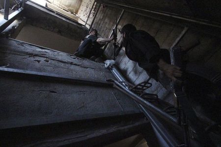 © Reuters. Rebel fighter hands weapon to fellow fighter as they move inside building on frontline in Damascus suburb of Harasta