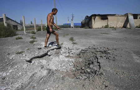 © Reuters. Local resident walks past a crater caused by shelling in the village of Spartak outside Donetsk