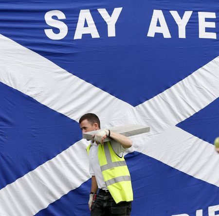 © Reuters. A workman walks past a Scottish saltire in Kilmarnock, Scotland