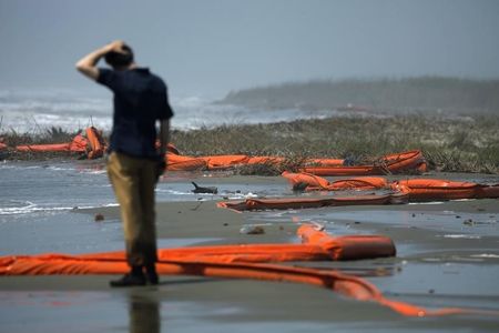 © Reuters. A television reporter stands beside oil booms at the coast of South Pass