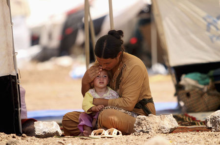 © Reuters. A refugee woman from the minority Yazidi sect, who fled the violence in the Iraqi town of Sinjar, sits with a child inside a tent at Nowruz refugee camp in Qamishli