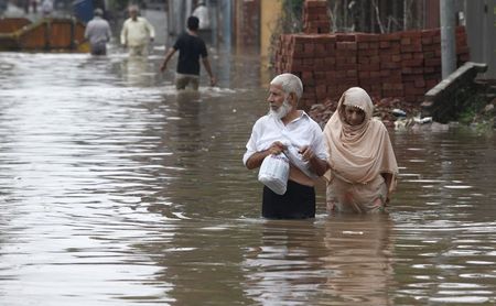 © Reuters. A couple wades through a flooded road after heavy rains in Lahore