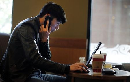 © Reuters. A man talks on the phone as he surfs the internet on his laptop at a local coffee shop in downtown Shanghai