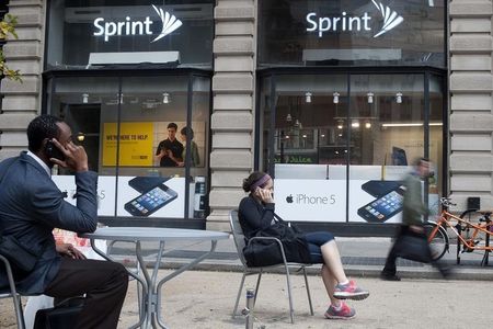 © Reuters. People talk on their cell phones as passers-by walk past a Sprint store in New York