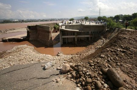 © Reuters. People stand on a damaged bridge which was swept away by floods on the river Tawi in Jammu