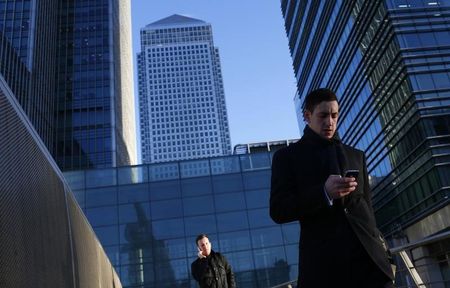 © Reuters. A worker looks at his phone at the Canary Wharf business district in London