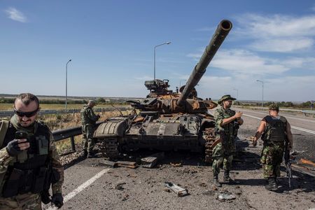 © Reuters. Pro-Russian rebels stand near a burnt-out Ukrainian tank outside the destroyed airport in Luhanks