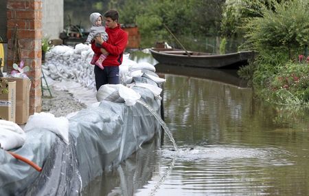 © Reuters. Un hombre toma en brazos a un bebé mientras miran a su jardín inundado en la aldea de Letovanic, en Croacia central