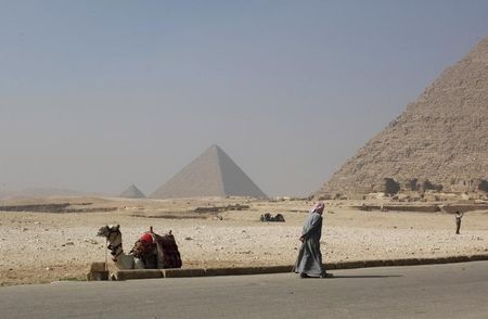 © Reuters. A worker walks near his camel as he waits for tourists at the Giza pyramids area south of Cairo