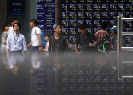 © Reuters. Pedestrians standing in front of an electronic board showing the various stock prices outside a brokerage are reflected in a polished stone surface, in Tokyo