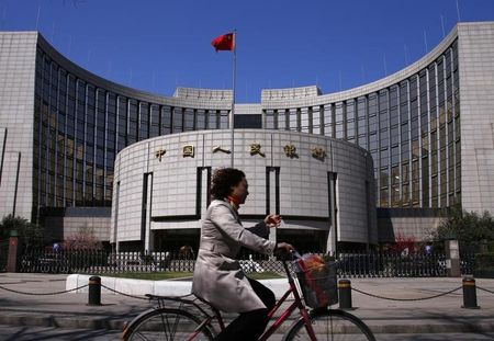 © Reuters. A woman rides past the headquarters of the People's Bank of China in Beijing