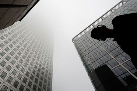 © Reuters. Man walks past a building in the morning mist at London's financial district of Canary Wharf