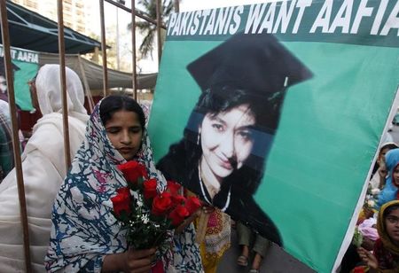 © Reuters. Aafia Siddiqui supporter carries silk roses next to a poster during a celebration to mark Siddiqui's 41st birthday in Karachi