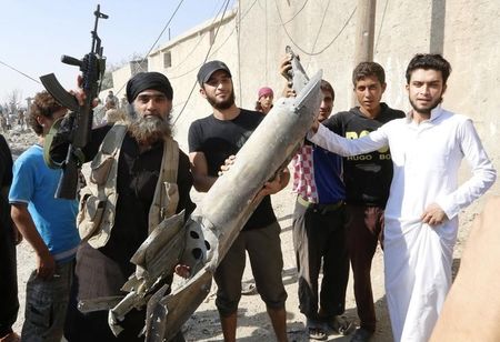 © Reuters. An Islamic State militant stands next to residents as they hold pieces of wreckage from a Syrian war plane after it crashed in Raqqa, in northeast Syria