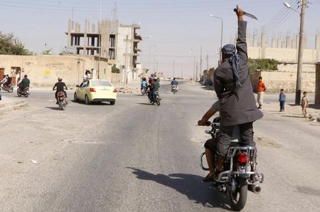 © Reuters. Man holds up a knife as he rides on the back of a motorcycle touring the streets of Tabqa city with others in celebration after Islamic State militants took over Tabqa air base, in nearby Raqqa city