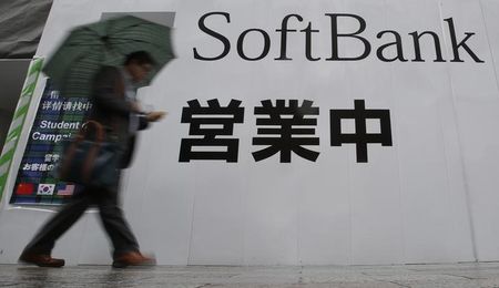 © Reuters. A man holding an umbrella walks past the logo of Softbank Corp at its branch in Tokyo