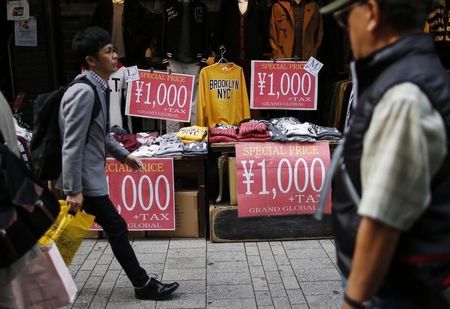 © Reuters. Shoppers walk past advertisement posters outside a clothing store at a shopping district in Tokyo