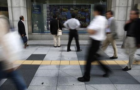 © Reuters. Pedestrians look at an electronic board showing the stock market indices of various countries outside a brokerage in Tokyo