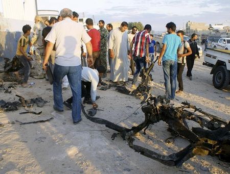 © Reuters. Pessoas caminham entre destroços após explosão de carro-bomba em Tobruk