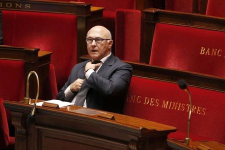 © Reuters. French Finance Minister Sapin adjusts his tie while seated at the start of debate on France's 2015 budget at the National Assembly in Paris