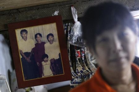 © Reuters. Than Dar, the wife of slain journalist Par Gyi, stands in front of a family photograph showing herself, her husband and daughter posing with Aung San Suu Kyi, during a Reuters interview at her home in Yangon