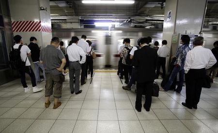 © Reuters. People stand to wait for a train on a platform at a train station in Tokyo