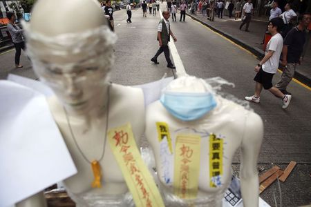 © Reuters. People walk behind mannequins decorated with symbols of the pro-democracy movement in the part of Mongkok shopping district protesters are occupying in Hong Kong
