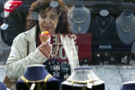 © Reuters. Woman eats ice cream as she looks at the display in the window of a Gold Standard jewellery store in New York