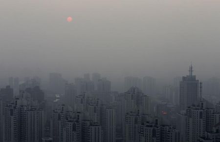 © Reuters. The sun sets above residential buildings on a hazy day in Beijing