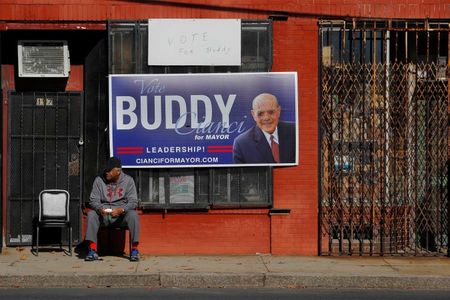 © Reuters. Man sits under a defaced campaign sign for independent mayoral candidate Cianci outside a campaign rally with United States first lady Obama and Democratic candidate for Rhode Island Governor Raimondo in Providence