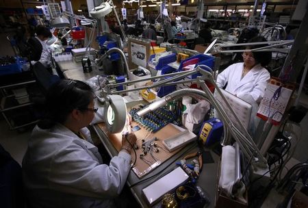 © Reuters. Workers use magnifying glasses as they work on components at the Rode Microphone factory located in western Sydney