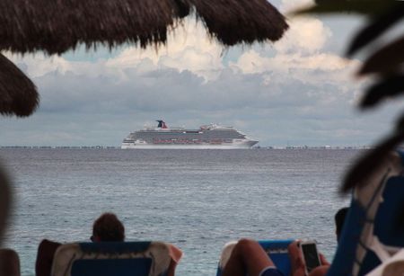 © Reuters. Tourists lie on the beach as cruise ship Carnival Magic is seen near the shores of Cozumel