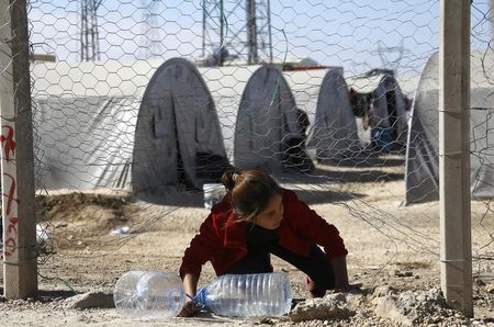 © Reuters. Kurdish refugee from the Syrian town of Kobani exits from an opening at the fence to collect water for her family at a refugee camp in the border town of Suruc