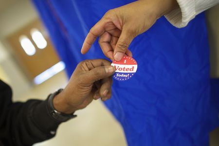 © Reuters. Voting machine operator Coffee-Ruff hands a sticker to a voter who cast his ballot at West Philadelphia High School on U.S. midterm election day morning in Philadelphia