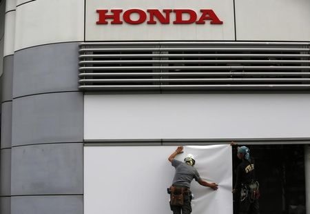© Reuters. Workers stand under the logo of Honda Motor Co. outside the company's headquarters in Tokyo