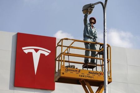 © Reuters. A labourer repairs street lamp next to logo of Tesla Motors in front of new showroom of the company in Shanghai
